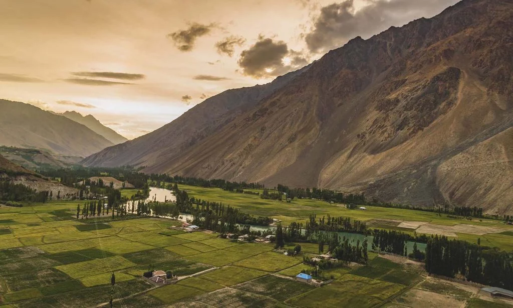 Phandar Valley Ghizer during golden with perfectly squared shape farm lands with green crops of Phander and a river piercing and flowing through it with a rocky brown mountain in the background
