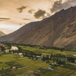 Phandar Valley Ghizer during golden with perfectly squared shape farm lands with green crops of Phander and a river piercing and flowing through it with a rocky brown mountain in the background