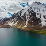 Karambar Lake in the foreground and a snow capped peak in the background with mostly cloudy sky captured from a drone