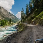 Off road jeep track on the right, glacial water river flowing parallel to the jeep track with lush green mountains on both sides and alpine trees on the way to Mahodand Lake from Kalam in Swat Valley