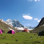 View of lush meadows with camps set up and snow capped mountains in the background during the Thallay la Trek