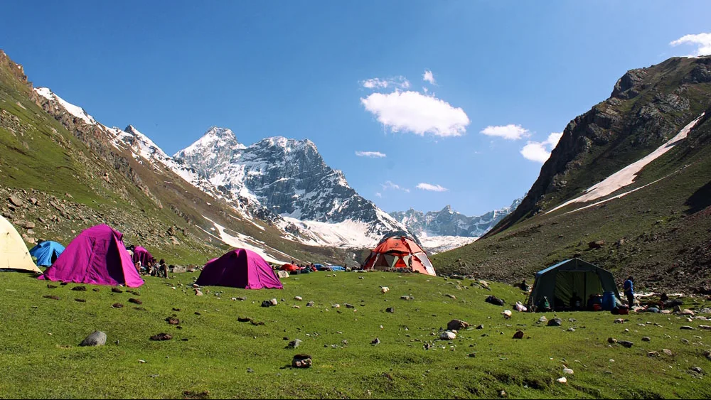 View of lush meadows with camps set up and snow capped mountains in the background during the Thallay la Trek. 